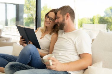 Evde güzel vakit. Güzel genç sevgi dolu çift bağ birbirlerine ve gülümseyen bir kitap kadın