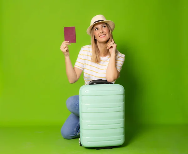 Young smiling woman with suitcase holding passport isolated over green background.