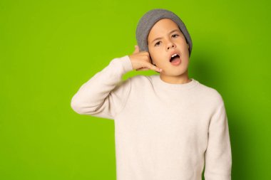 Çocuk portresi parmaklarıyla telefon işareti yapıyor, yeşil arka planda izole edilmiş.