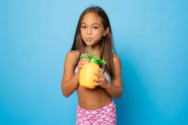 Mavi arka planda ananas tutan mayo giymiş gülümseyen bir kızın portresi. Seyahat kavramı