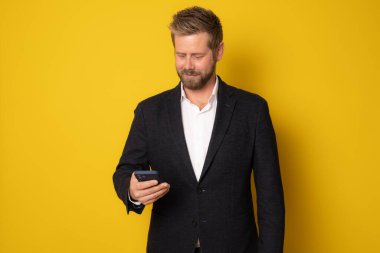 Sarı arka planda cep telefonu kullanan gülümseyen genç bir iş adamı..