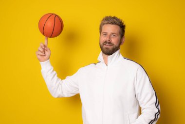 Sarı arka planda izole edilmiş basketbol topu olan genç bir adam..