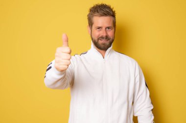 Genç sporcu, sarı arka planda başparmağını kaldırmış duruyor..