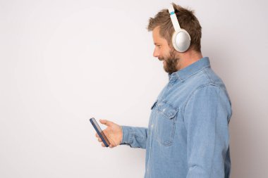 Kulaklıklı genç adamın profili sarı arka planda izole halde duran akıllı telefon kullanıyor..