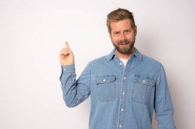 Kot gömlekli genç adam beyaz arka planda parmak kaldırıyor..