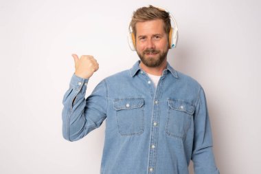 Genç gülümseyen, kulaklık takan, beyaz arka planda baş parmağını kaldıran sıradan bir adam..