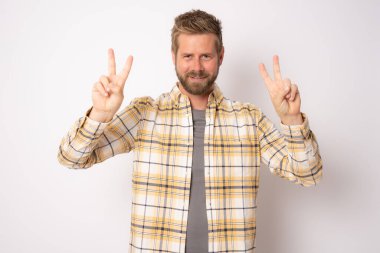Sakallı, ekose gömlekli yakışıklı genç adam kameraya bakıp zafer işareti yapıyor..