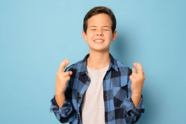 Mavi arka planda izole edilmiş şans jestli ekose gömlek giyen çocuk..