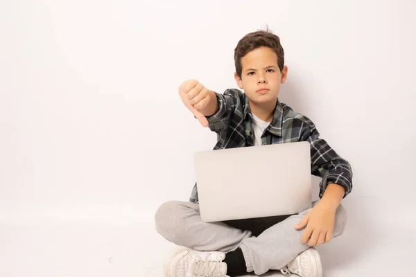 Poważny Chłopiec Kratę Siedzi Podłodze Trzymając Laptopa Kciukiem Dół Odizolowany — Zdjęcie stockowe