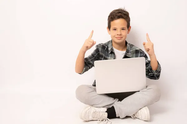 Uśmiechnięty Chłopak Noszący Koszulę Kratę Siedzący Podłodze Laptopem Wskazującym Palcem — Zdjęcie stockowe