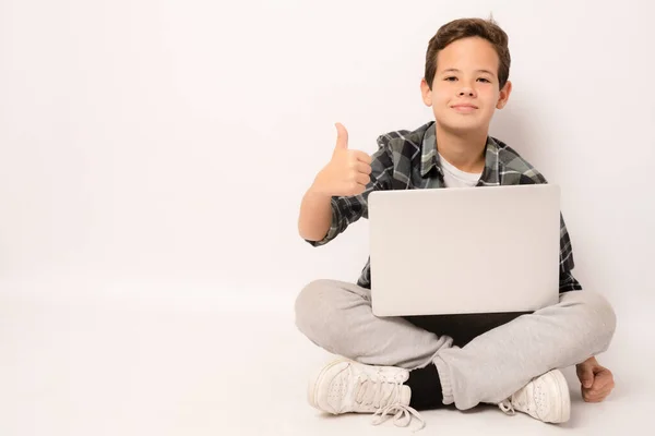 Uśmiechnięty Chłopak Noszący Koszulę Kratę Siedzi Podłodze Trzymając Laptopa Kciukiem — Zdjęcie stockowe