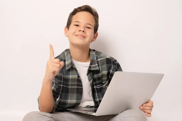 Uśmiechnięty Chłopak Noszący Koszulę Kratę Siedzący Podłodze Laptopem Wskazujący Palcem — Zdjęcie stockowe