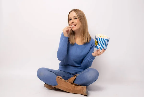 Młoda Kobieta Niebieskim Swetrze Siedząca Podłodze Jedząca Popcorn Białym Tle — Zdjęcie stockowe