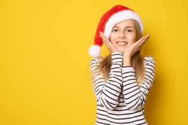 Sarı arka planda izole edilmiş, Noel Baba şapkalı şirin kız portresi..