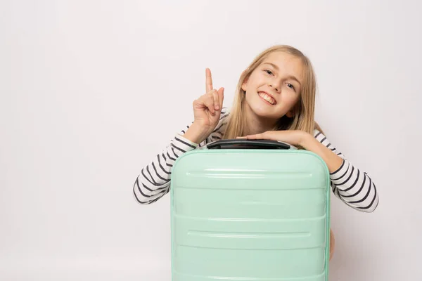 Χαριτωμένο Χαμογελαστό Κορίτσι Κρατώντας Πράσινη Βαλίτσα Δείχνοντας Δάχτυλο Προς Πάνω — Φωτογραφία Αρχείου