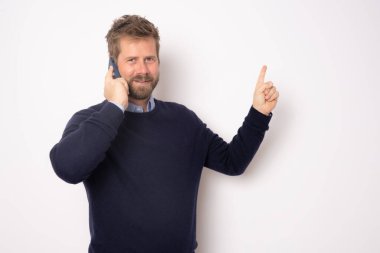 Genç, gülümseyen, telefonda konuşan, beyaz arka planda yalnız bir şekilde duran, parmağını kaldıran yakışıklı adam..