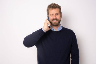 Genç gülümseyen yakışıklı adam cep telefonuyla konuşuyor beyaz arka planda tek başına duruyor..