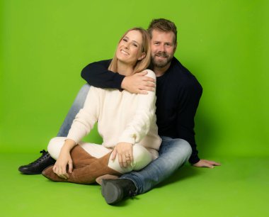 Birbirini seven çift yeşil arka planda zemin üzerinde sırt sırta oturuyor..