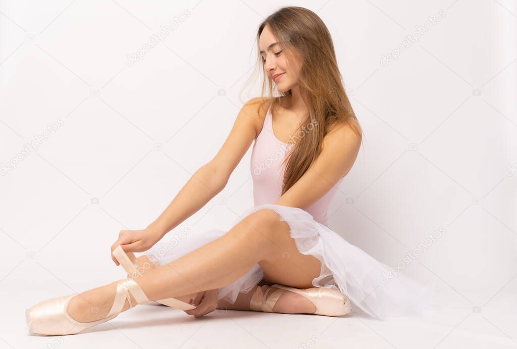 Photo of amazing woman ballerina sitting over white wall background isolated.