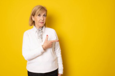 Kıdemli kadın sarı arka planda izole edilmiş bir şekilde işaret ediyor..