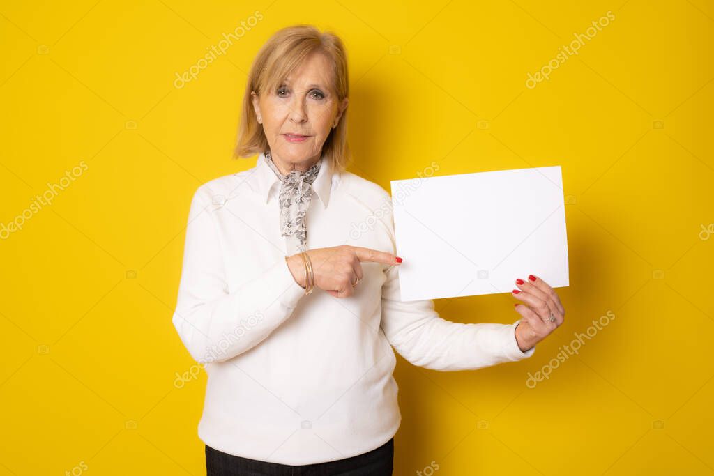 Senior woman holding blank signboard isolated over yellow background