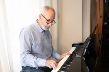 Yaşlı adam evde piyano çalıyor.