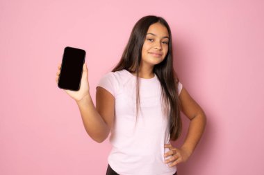 Uzun saçlı mutlu genç kız pembe arka planda boş cep telefonu tutuyor.