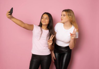 Sıradan giyinmiş iki neşeli kızın portresi pembe arka planda izole edilmiş bir selfie çekiyor..