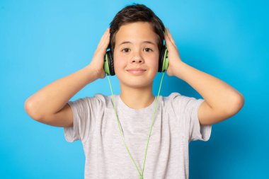Kulaklık takan sevimli çocuk mavi arka planda izole edilmiş müzik dinliyor..