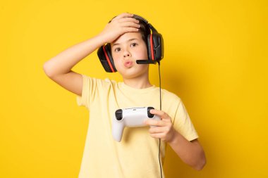 Çocuk video konsoluyla oynarken eğleniyor. Sarı arkaplanda izole edilmiş.