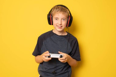 Çocuk video konsoluyla oynarken eğleniyor. Sarı arkaplanda izole edilmiş.