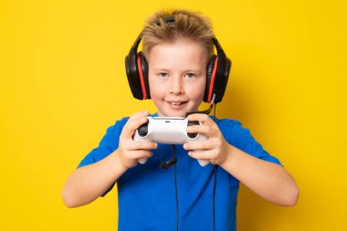 Çocuk video konsoluyla oynarken eğleniyor. Sarı arkaplanda izole edilmiş.