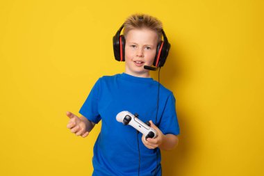 Çocuk video konsoluyla oynarken eğleniyor. Sarı arkaplanda izole edilmiş.