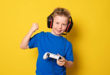 Çocuk video konsoluyla oynarken eğleniyor. Sarı arkaplanda izole edilmiş.