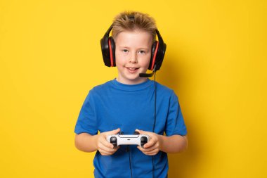 Çocuk video konsoluyla oynarken eğleniyor. Sarı arkaplanda izole edilmiş.