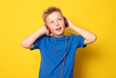 Kulaklık takan sevimli çocuk sarı arka planda izole edilmiş müzik dinliyor..