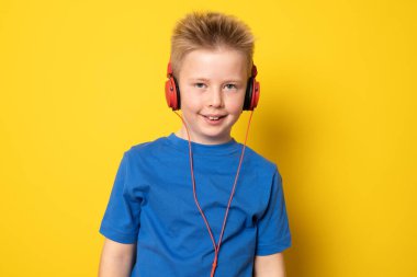 Kulaklık takan sevimli çocuk sarı arka planda izole edilmiş müzik dinliyor..