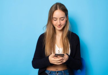Beautiful girl using smartphone sitting isolated over blue background.