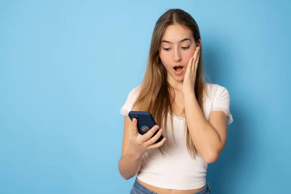 Amazedl Girl Using Smartphone Standing Isolated Blue Background — Stockfoto