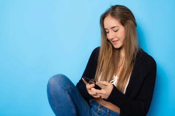 Beautiful Girl Using Smartphone Sitting Isolated Blue Background — Stockfoto