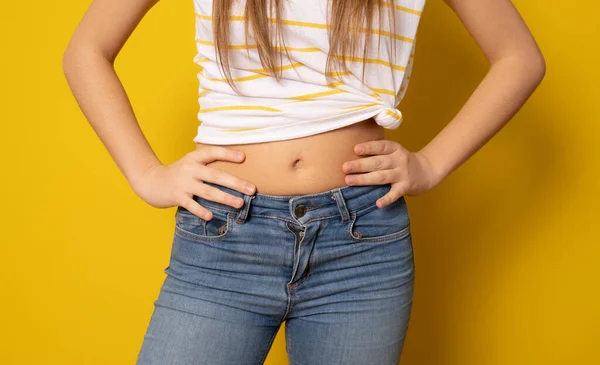 Close up of flat abdomen of young woman in ripped jeans isolated over yellow background.