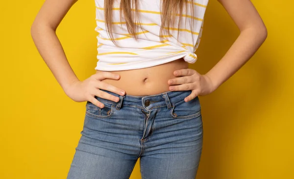 Close up of flat abdomen of young woman in ripped jeans isolated over yellow background.