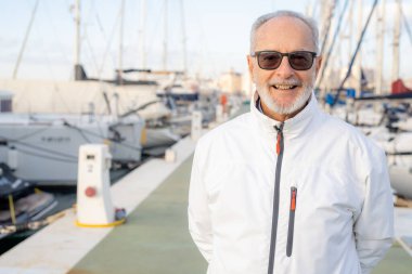 Elderly smiling man spending free time walking on marina.