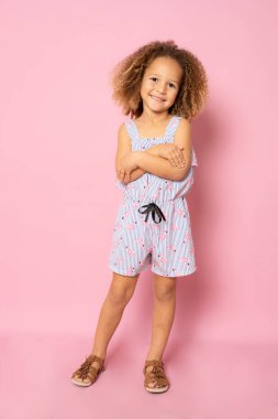 Full length photo of excited charming cute little girl with her hands folded standing over pink background.