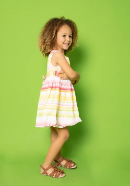 Full length photo of excited charming cute little girl with her hands folded standing over green background.