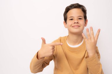 Küçük çocuk gündelik giysiler giyer ve parmaklarıyla dört numarayı gösterirken kendinden emin ve mutlu bir şekilde gülümser..