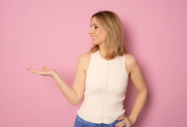 Gülümseyen kadın pembe arka planda el ele duran ürünleri gösteriyor..