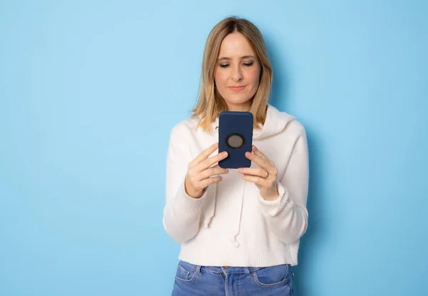 Młoda Kobieta Pomocą Smartfona Stojącego Niebieskim Tle — Zdjęcie stockowe