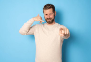 Genç sakallı adam bana jest diyor. Mavi arka planda tek başına duruyor..