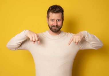 Sarı arka planda izole edilmiş genç adam parmakları aşağıda, olumlu hisler içinde..